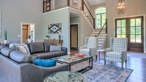 A spacious living room with a large sectional sofa, two patterned armchairs, a glass coffee table, and a staircase leading to an upper level. - Luxury Estate w/ Hot Tub & Game Room + Biltmore Pass | 18 Min to Asheville (Asheville)