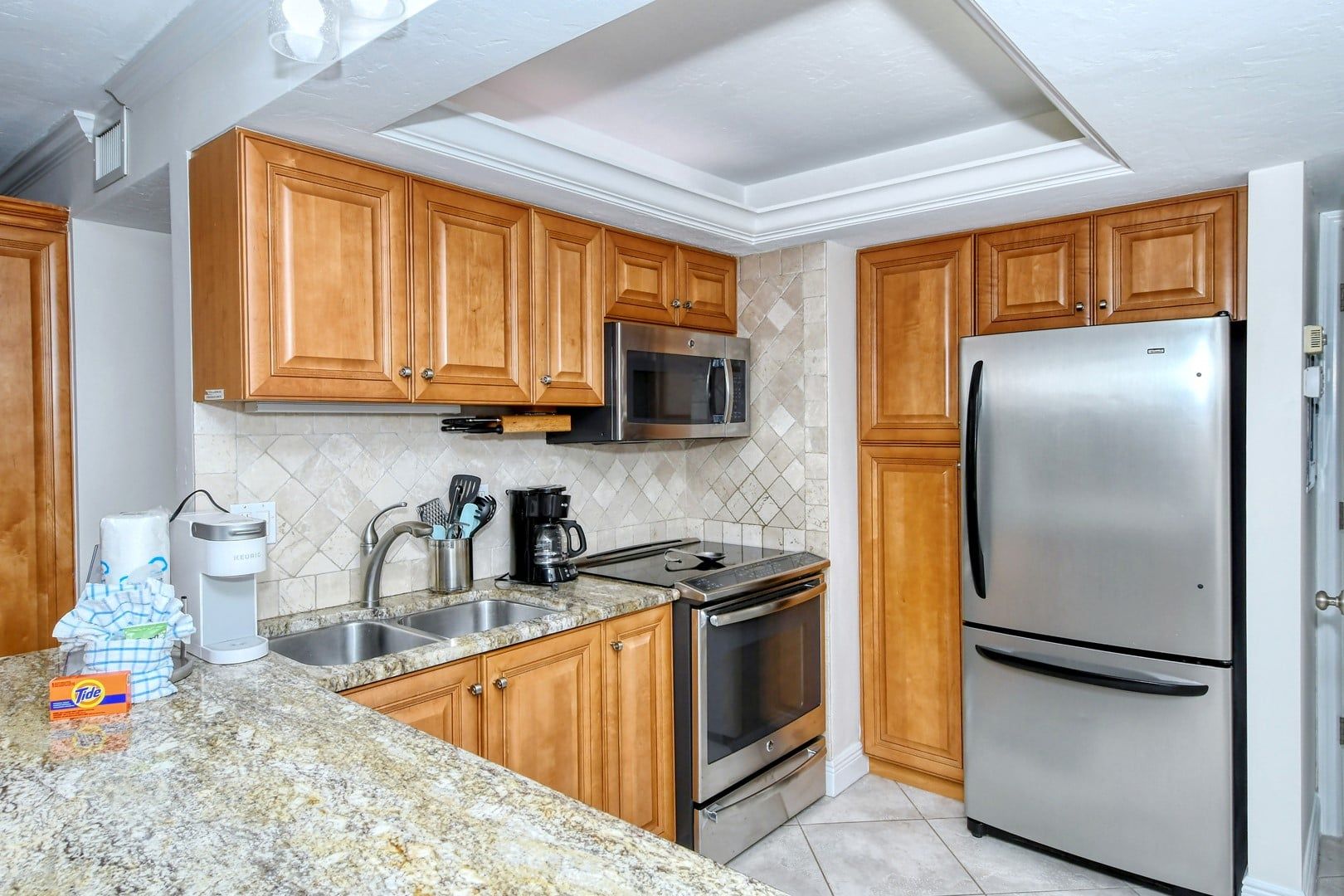 A kitchen with wooden cabinets, stainless steel appliances, a granite countertop, and a tiled backsplash.