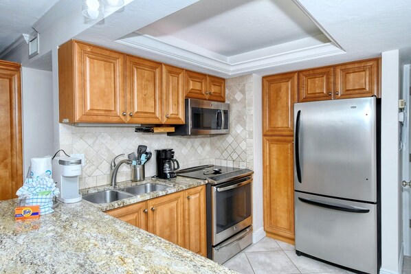 A kitchen with wooden cabinets, stainless steel appliances, a granite countertop, and a tiled backsplash. - Firethorn 210- Beautiful gulf side, ground-level 2BR/2BA unit! (Sarasota)