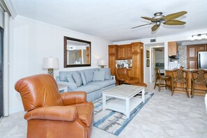 A living room with a sofa, a leather armchair, a coffee table, and a ceiling fan. - Firethorn 210- Beautiful gulf side, ground-level 2BR/2BA unit! (Sarasota)