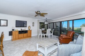 A spacious living area with a dining table, chairs, a sofa, a coffee table, and a TV mounted on the wall. - Firethorn 210- Beautiful gulf side, ground-level 2BR/2BA unit! (Sarasota)