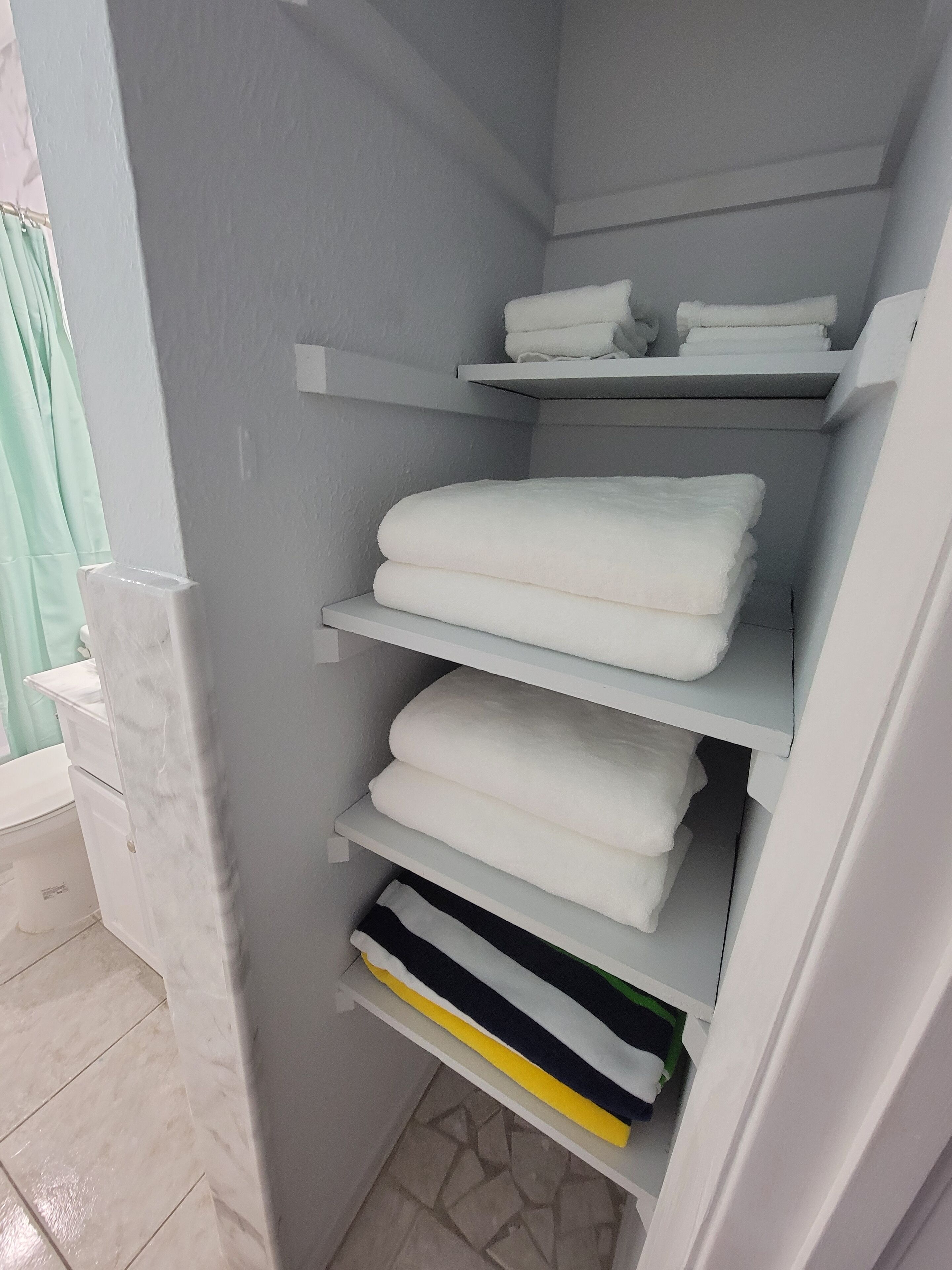 A bathroom with a white marble sink, a white towel rack with folded towels, and a white storage unit with towels and a green item.