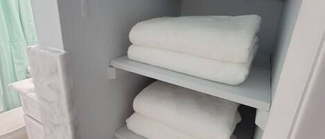 A bathroom with a white marble sink, a white towel rack with folded towels, and a white storage unit with towels and a green item.