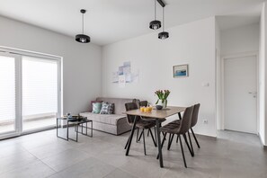 Een moderne woonkamer met een bank, eettafel en stoelen. Er hangen kunstwerken aan de muur en staat een vaas met bloemen.
