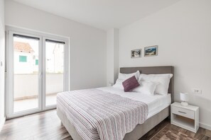 Een slaapkamer met een bed, een nachtkastje, een raam met zonwering en uitzicht op buiten.