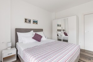 Quarto moderno com uma cama grande, uma mesinha de cabeceira, um guarda-roupa e duas molduras na parede.
