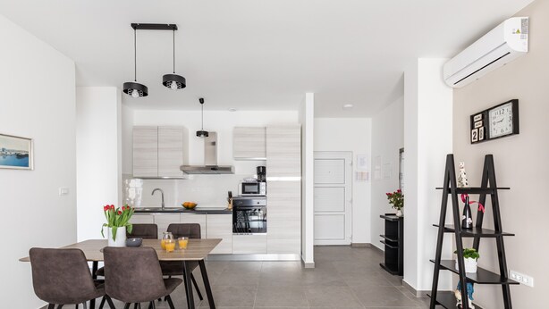 A modern kitchen with white cabinets, a dining table with chairs, and a black shelf unit. - Apartments Villa Salona Sky - Premium One Bedroom Apartment with Balcony (Solin)