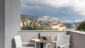 A balcony with two white wicker chairs, a table with a book, a basket of bread, and glasses of orange juice. - Apartments Villa Salona Sky - Premium One Bedroom Apartment with Balcony (Solin)