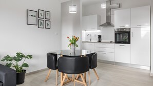 A modern kitchen with white cabinets, a built-in oven, and a dining area with a glass table and black chairs.