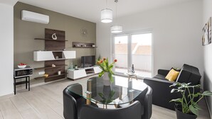 A modern living room with a glass dining table, black sofas, and a large window.