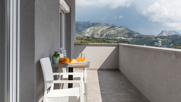 A balcony with a table and chairs, a potted plant, and a view of mountains.
