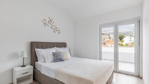 A bedroom with a bed, nightstand, and a view of the outside through a sliding door. - Apartments Villa Salona Sky - DeluxeTwo Bedroom Apartment with Balcony (Solin)