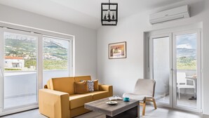A modern living room with a sofa, a coffee table, and a chair. There are large windows offering a view of a mountainous landscape. - Apartments Villa Salona Sky - DeluxeTwo Bedroom Apartment with Balcony (Solin)