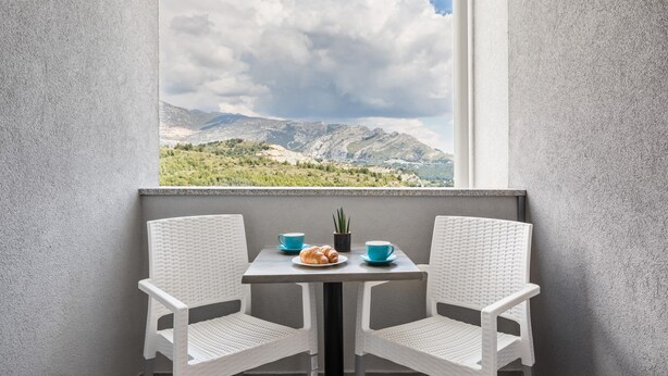 A balcony with two white wicker chairs, a small table, and a view of mountains and greenery. - Apartments Villa Salona Sky - DeluxeTwo Bedroom Apartment with Balcony (Solin)