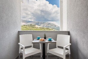 Un balcón con dos sillas de mimbre blancas, una mesita y vistas a montañas y vegetación.