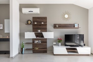 Una sala de estar moderna con un televisor de pantalla plana, estanterías de madera, un espejo decorativo con diseño de sol y una planta en maceta.