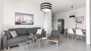 A modern living room with a grey sofa, a dining area with white chairs, and a kitchen in the background. - Apartments Villa Salona Sky - Superior Two Bedroom Apartment with Balcony (Solin)