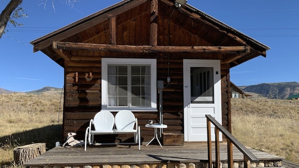 A rustic log cabin with a wooden deck, two white chairs, and a small table.