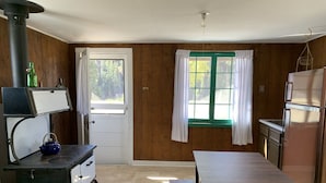 A compact kitchen with a stove, sink, and refrigerator. There's a window with curtains and a door leading outside.