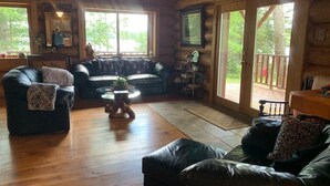 A log cabin interior with a wooden floor, two leather sofas, a small round table, and a dog. - Private, Family/Pet-Friendly, Log Cabin on Waterfront Chicaugon Lake Property.   (Crystal Falls)