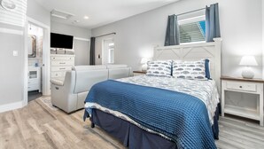 A bedroom with a bed, a TV, a desk, and a chair.