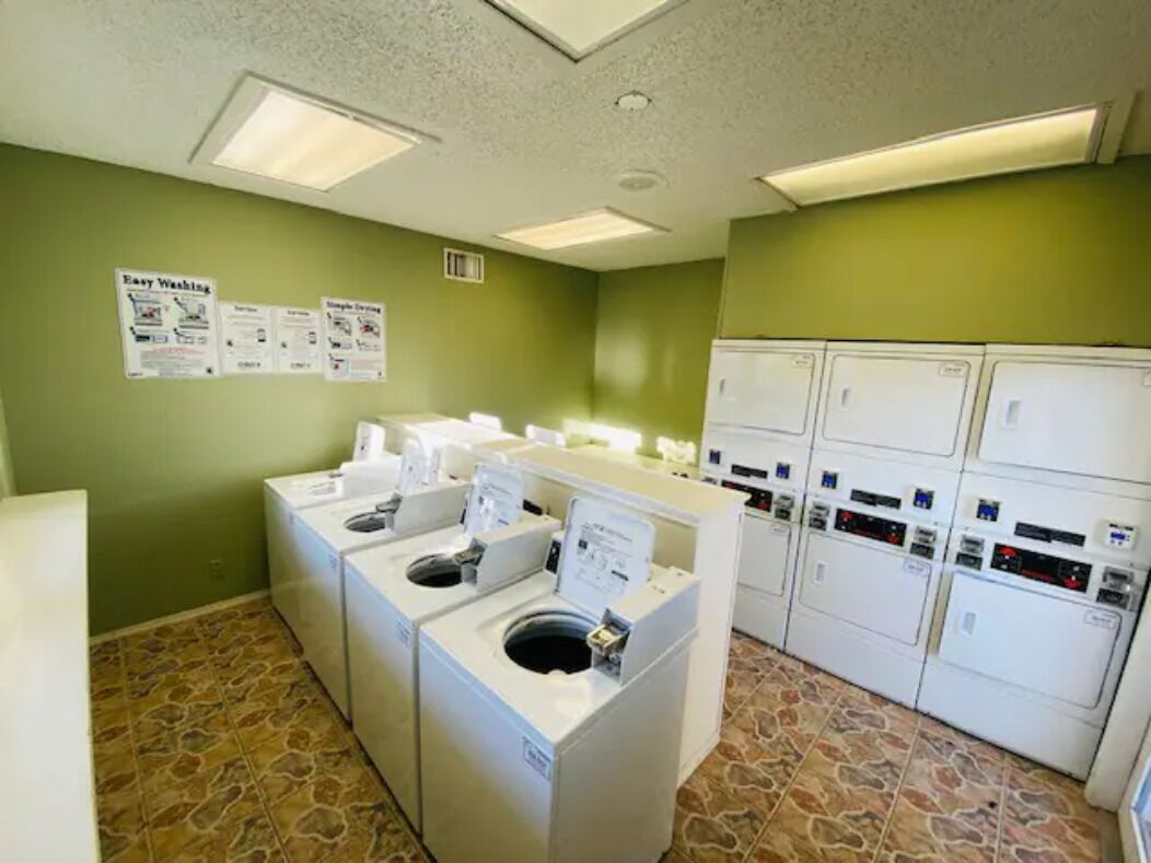 A laundry room with multiple washing machines and dryers, green walls, and a tiled floor.