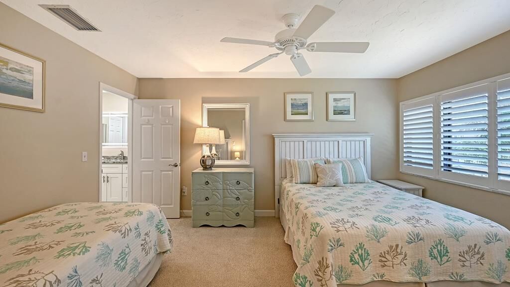 A bedroom with two beds, a ceiling fan, a dresser, and a window with blinds.