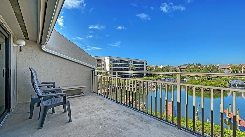 A balcony with two chairs, a view of a body of water, and a building in the background.