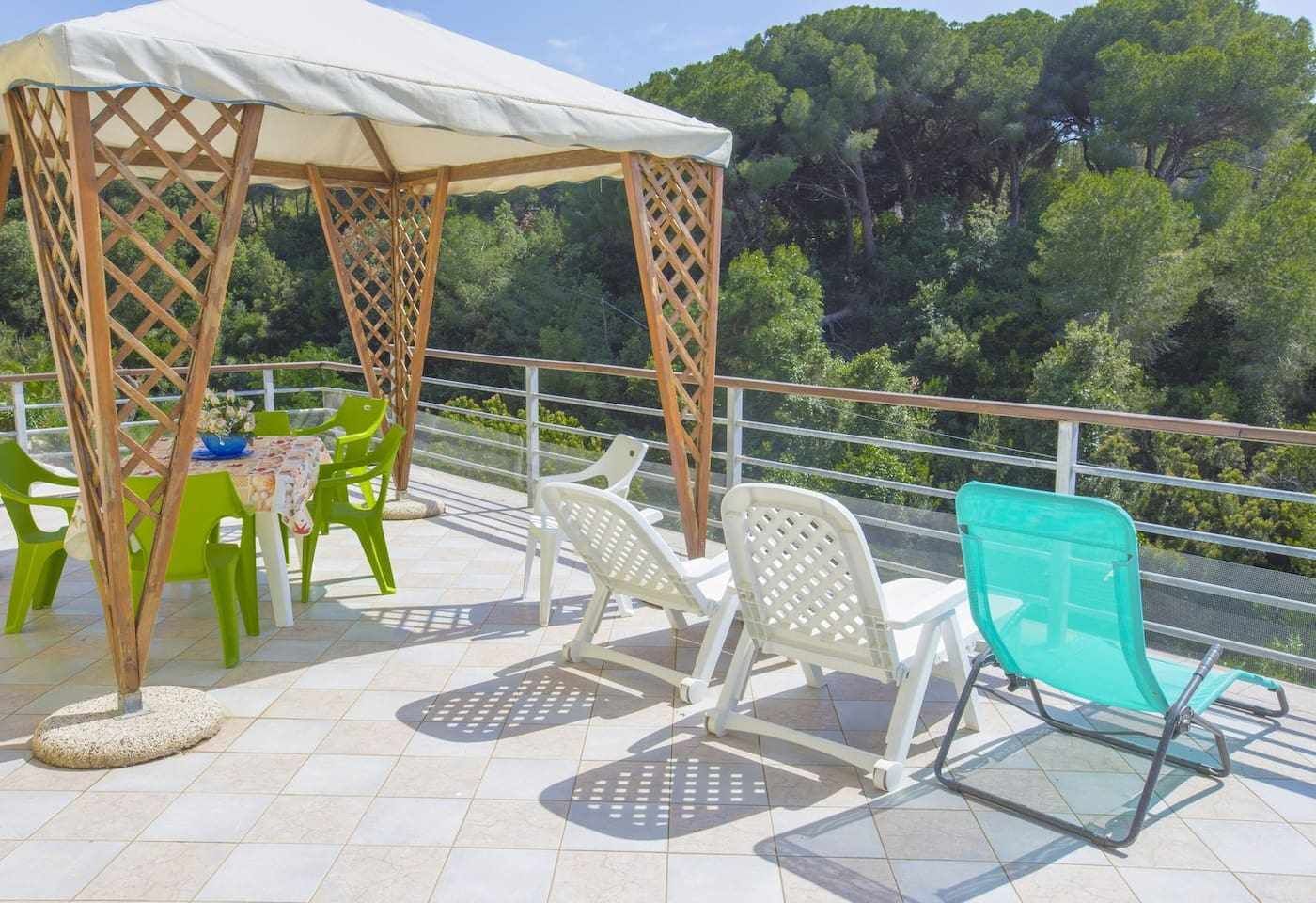 Un espace extérieur abrité, doté d’une table et de chaises, entouré d’une rambarde et offrant une vue sur une zone boisée.