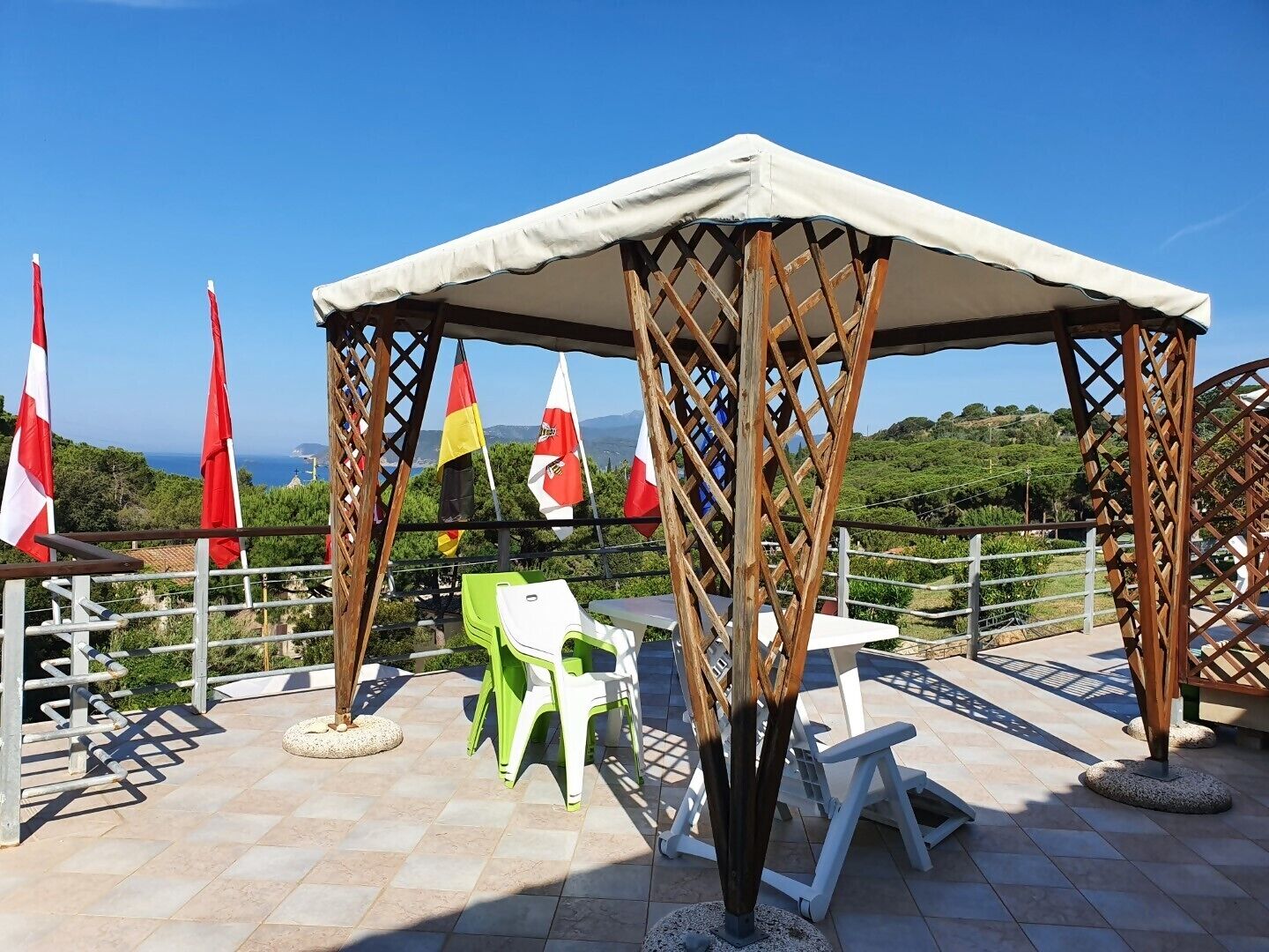 Ein überdachter Außenbereich mit Meerblick, Flaggen und einer Pergola.