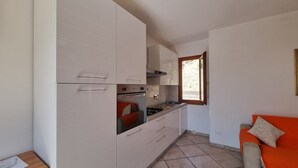 Une cuisine de taille réduite avec des meubles blancs, une cuisinière et une fenêtre.