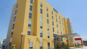 Ein mehrgeschossiges Hotel mit gelber Fassade, einem überdachten Eingang und einer rot-weißen Beschilderung.