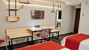 Ein Hotelzimmer mit Bett, Schreibtisch, Stuhl, Fernseher und Spiegel.