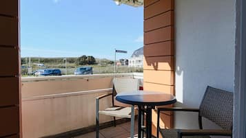 En balkon med et bord og to stole, udsigt til en parkeringsplads og en bygning i baggrunden.