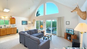 Een ruime woonkamer met een hoekbank, een opgehangen hertenkop, een televisie en een eethoek met tafel en stoelen.
