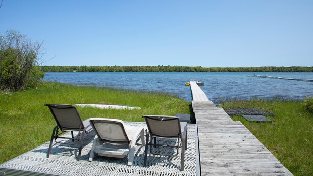 Een houten steiger die uitkomt bij een rustig meer, met twee ligstoelen gericht op het water.