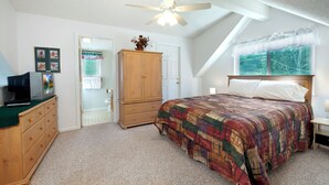 Een slaapkamer met een bed, een houten garderobe, een televisie op een dressoir en een raam met uitzicht op bomen.