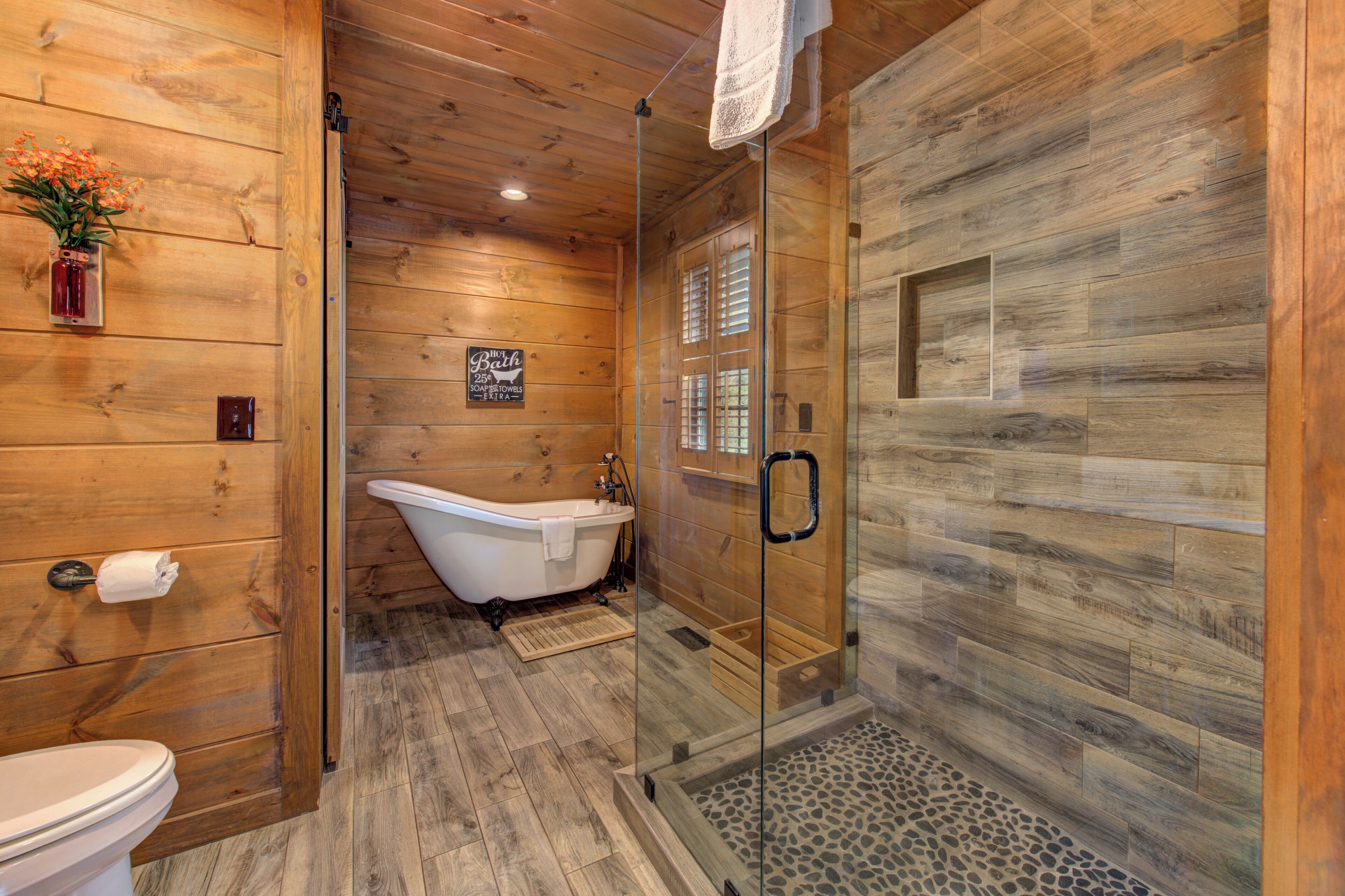 A wooden interior with a glass-enclosed shower, a white bathtub, and a toilet.