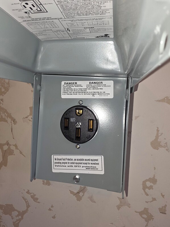 A wall-mounted electrical outlet with a warning label and a grounding protection sticker.