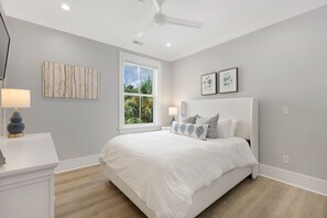 A bedroom with a bed, a ceiling fan, a window, and artwork on the walls.