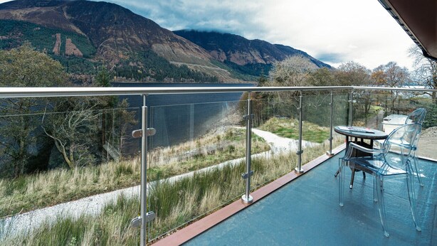 A balcony with a clear view of mountains, a glass table, and two chairs.