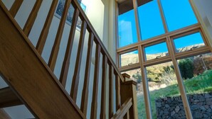 A wooden staircase with a view of a stone wall and a clear blue sky through large windows.