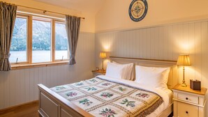 A bedroom with a bed, two bedside tables, a window with curtains, and a wall clock.