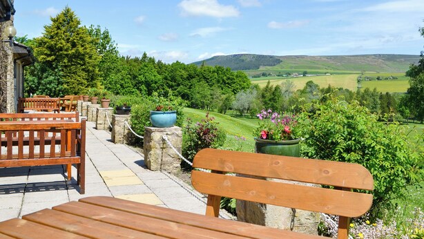 A patio with wooden benches and stone pillars, overlooking a lush valley with rolling hills and a clear sky. - Enviable location within the golf course. (Skipton)