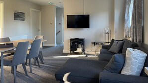 A modern living room with a flat-screen TV mounted on the wall, a fireplace, a sofa, and a dining area with chairs. - Enviable location within the golf course. (Skipton)