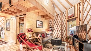 A cozy cabin interior with a wooden floor, a sofa, a red chair, a TV, and a fireplace. - Lush Comfort, great for couples or small family, Huge Deck w/Privte Hot Tub (Pigeon Forge)