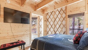 A wooden cabin interior with a bed, a bench, a TV mounted on the wall, and a lattice window. - Lush Comfort, great for couples or small family, Huge Deck w/Privte Hot Tub (Pigeon Forge)