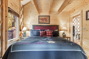 A wooden cabin bedroom with a bed, a headboard, a window, and a wall-mounted picture.