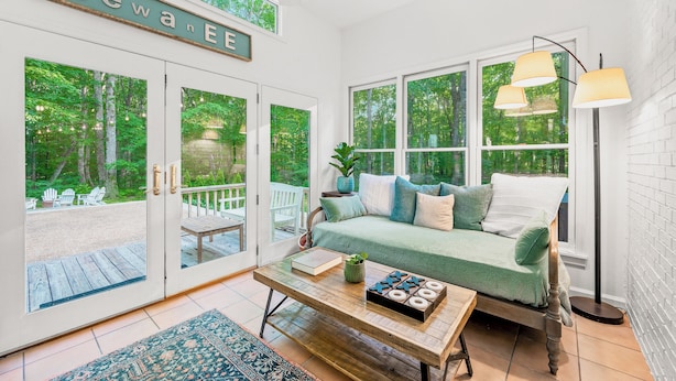 A cozy room with a green sofa, a wooden coffee table, and a view of a deck and forest through large windows.