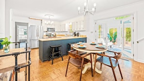 A modern kitchen with a central island, wooden flooring, and a dining area with a round table and chairs.
